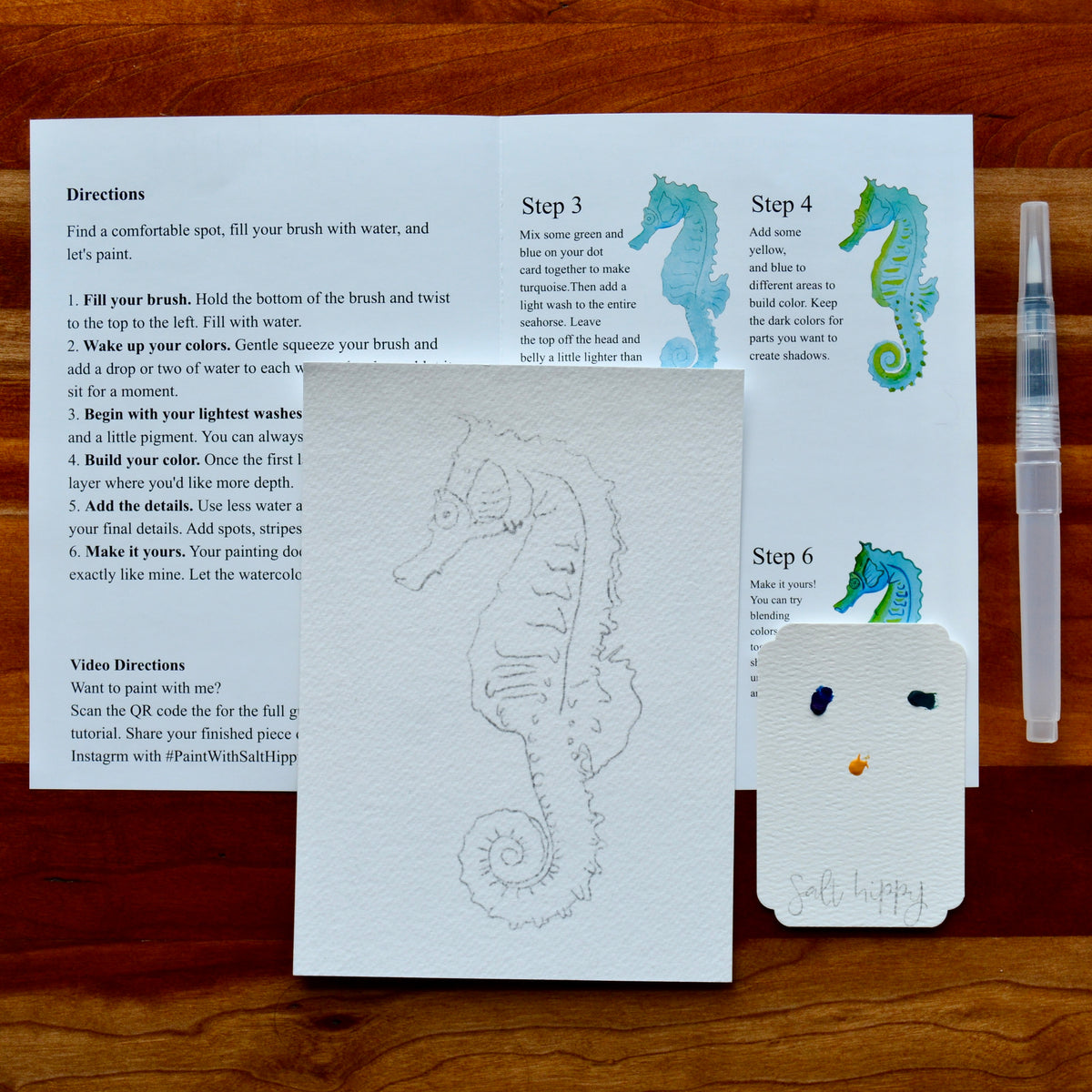 A set of painting and brush-stroke instruction cards laid out on a wooden surface, alongside a small paint palette and a paintbrush. The cards show numbered steps from Step 1 to Step 6 with painted examples of seahorse and abstract designs.